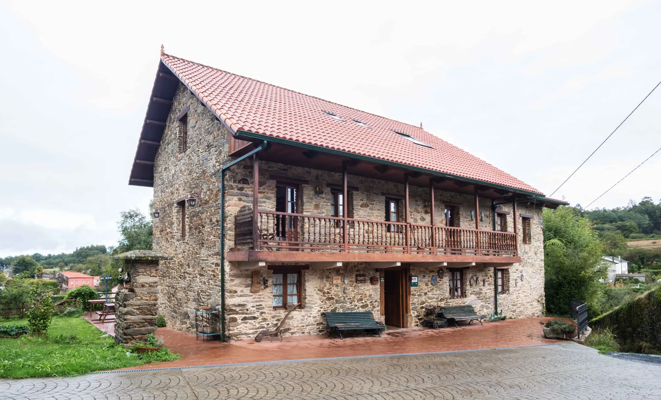 Fachada de piedra de Casa de Sixto con tejado de teja roja y galería de madera