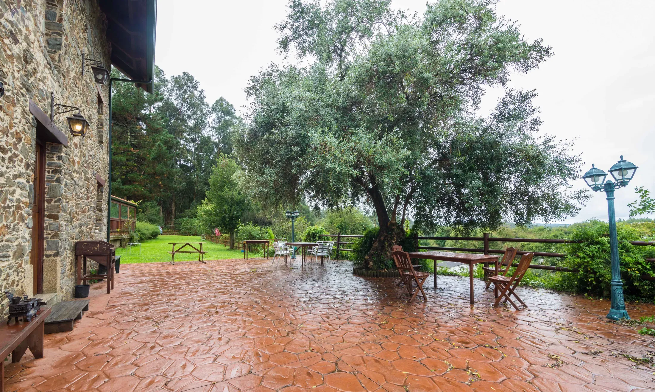 Terraza exterior con suelo de ladrillo, mesa de madera y jardín