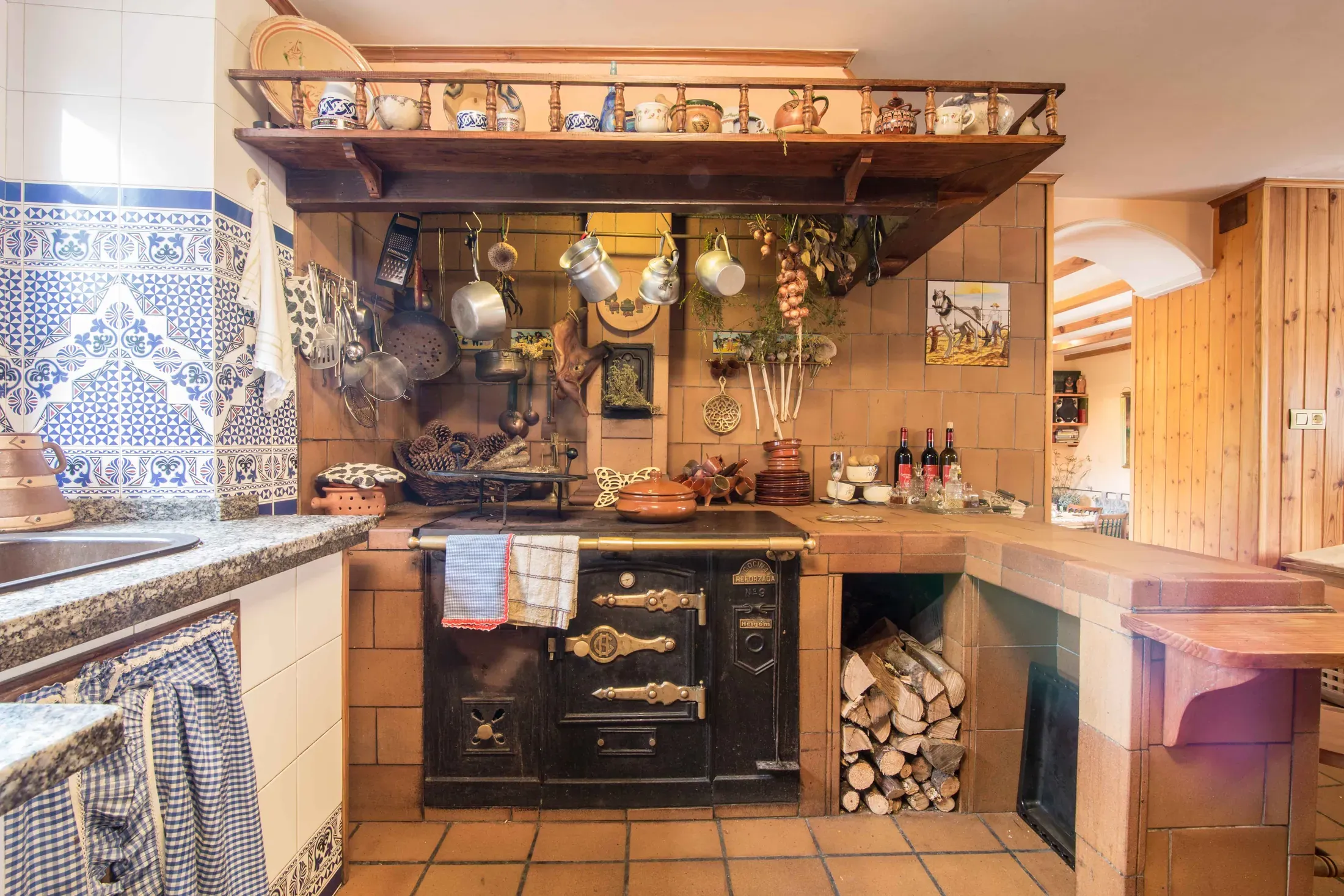 Rincón de la cocina con cocina económica de leña, ollas de cobre y leña apilada