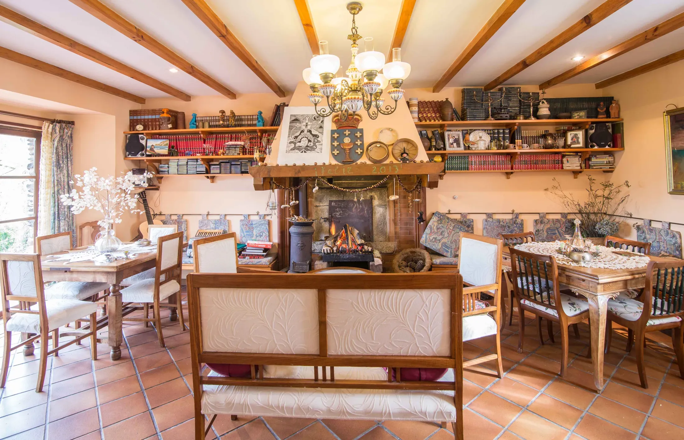 Salón con chimenea de piedra, lámpara de araña y estanterías con la vajilla