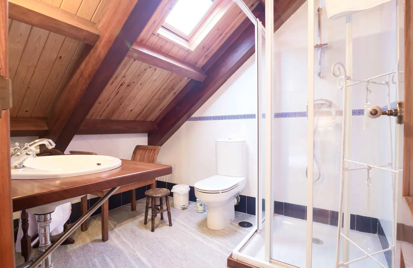 Baño con ducha angular y lavabo de madera bajo el techo de vigas